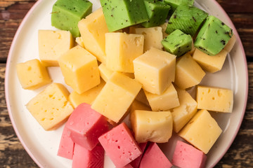 Cheese cubes of green, yellow and red on a plate. View top. Close up