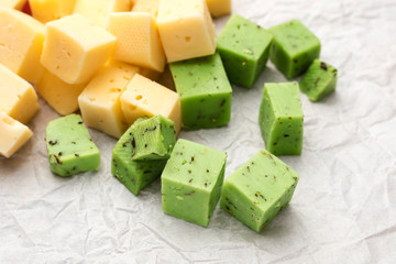 Cheese cubes of green and yellow on crumpled paper background. Cheese Pesto Closeup