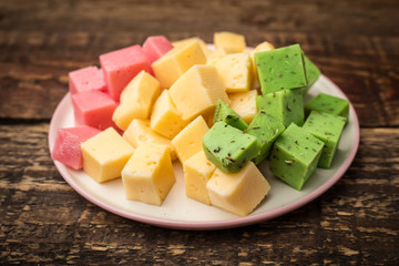 Cheese cubes of green, yellow and red on a plate. Wooden background
