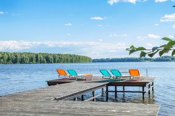 Empty bright sunbeds on wooden pier by the river. Concept of tourism and recreation.