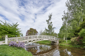Fototapeta na wymiar Beautiful landscape with a small river and a white bridge on the background of trees in a city park in the city of Baden Baden, Germany, Europe. Bridge and river in Lichtentaler Allee park