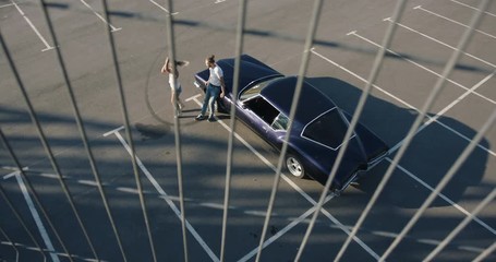 HIGH ANGLE view of Caucasian couple standing near old classic vintage 70s muscle car on a parking lot. Automotive lifestyle