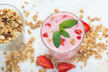 A glass of healthy strawberry yogurt with fresh berries, muesli and mint on a white wooden table. Healthy breakfast.