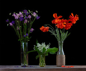 bouquet of red poppies, a bouquet of white lilies of the valley and a bouquet of flowers bells in glass vases on a black background close-up