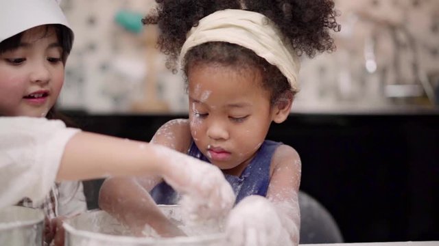 Slow motion - Group of children baking cake together in classroom, Multi-ethnic young boys and girls happy making dessert cooking in kitchen at school. Kids cooking at school concept.