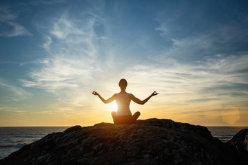 Silhouette young woman practicing yoga on the sunset beach. Tranquility and concentration..