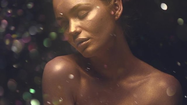 Beautiful sexy girl with golden skin. Fashion model woman in golden bright sparkles posing in studio. Creative metallic gold makeup. Slow motion 4K UHD video footage. 3840X2160