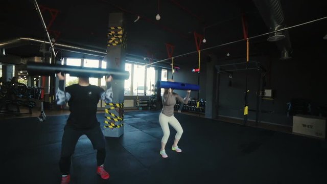 strong couple squats holding special weights in hands in modern sports club with columns and windows slow motion