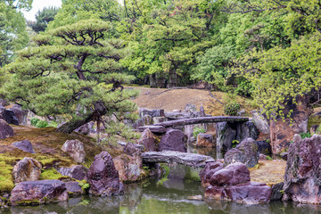 Fototapeta na wymiar Beautiful scenery at Nijo Castle. View of the formal gardens, with a pond and stone bridges. On a rainy day, droplets are visible in the air.