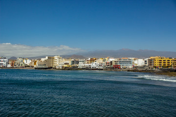 Fototapeta premium Wide angle panorama View of the volcanic beach towards the resort hotels, restaurants and terraces, in the bohemian village of El Medano in Granadilla de Abona, Tenerife.