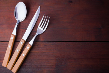 Rustic set of cutlery knife, spoon, fork. Dining set with wooden handles. Wooden background. Copy space. Top view