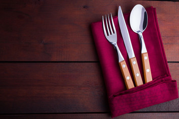 Rustic set of cutlery knife, spoon, fork. Сutlery with burgundy napkin and twine. Wooden background. Copy space. Top view