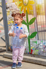 Naklejka premium Little Girl Recycling Plastic Water Bottles. Crate of plastic water bottles ready for recycling in bin. Concept of awareness of the plastic pollution world, the future for our children. Zero waste.