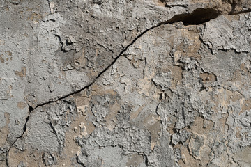Old textured concrete wall with traces of putty, peeling paint and large cracked.