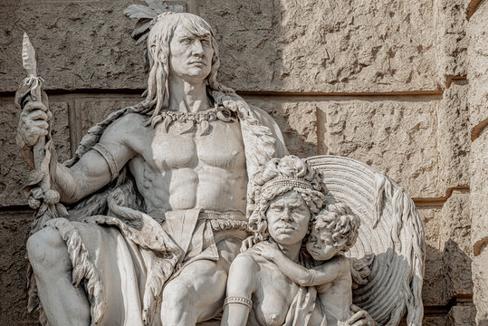 Old Symbolic Statue Of Indigenous People Of America And Australia, Inca Or Indian Warier With Spire And Aborigine Woman With A Child Located In Museums District, Downtown In Vienna, Austria