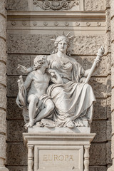 Fototapeta na wymiar Old symbolic statue of Europa, a powerful woman with torch and young boy with musical instrument and easel for painting located in museums district, downtown in Vienna, Austria