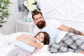 Obraz na płótnie Canvas Guy and girl relaxing in bedroom. Pajamas style. Having fun pajamas party. Happy fatherhood. Man bearded hipster with childish hairstyle colorful ponytails and daughter in pajamas. Slumber party