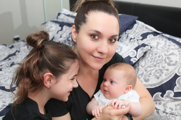 Close up portrait of Young Beautiful Mother with two daughters, Cute 3 Month Old Baby Girl , 7 Years Old Girl, Happy Family, Happy Mother’s Day, Best Mother Concept, The Most Beautiful Girls in the wo