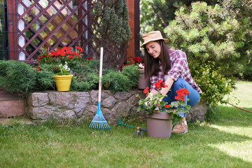 Beautiful smiling Caucasian brunette in working clothes and with hat pruning flowers in her...