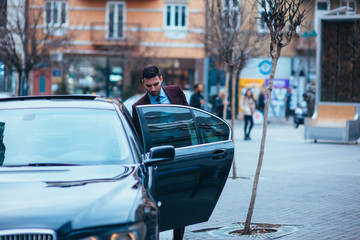 Entrepreneur(Businessman) standing in an urban area and wearing a suit and tie next to his limo while talking on the phone.