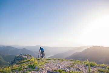 Mountain biker holding his bike on a rough cliff terrain on a sunset.