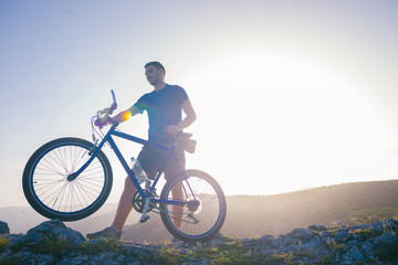 Fototapeta na wymiar Mountain biker holding his bike on a rough cliff terrain on a sunset.