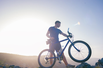 Mountain biker holding his bike on a rough cliff terrain on a sunset.