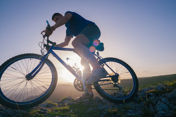 Fototapeta na wymiar Strong fit male mountain biker performing stunts on rocky terrain on a sunset while wearing a blue shirt and riding a blue bike