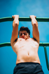 Attractive man pull-ups on a bar against blue sky