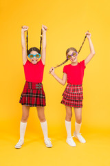 Fototapeta premium Summer fashion trend. Kids fashionable friends posing in sunglasses on yellow background. Summer fun. Summer accessory. Girls cute sisters similar outfits wear colorful sunglasses for summer season