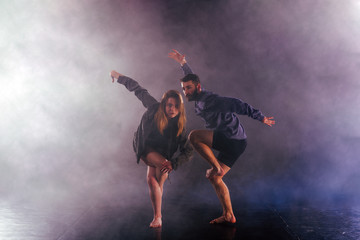 Two modern dancers stretching their shoeless feet high in the air surrounded by smoke on stage.