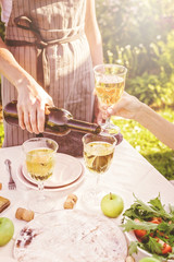 Woman pouring white wine. Dinner concept with wine in the fresh air. Fish and salads with vegetables and herbs. Mediterranean Kitchen. Vertical shot