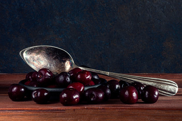 CHERRIES AND ANTIQUE METAL SPOON ON WOODEN TABLE