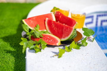 Summer holiday tropical concept. Fresh orange juice and watermelon juice and pineapple on border of a swimming pool.