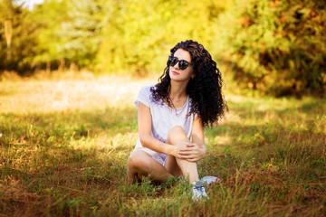 Naklejka na ściany i meble Pretty curly woman posing on grass in sunny day