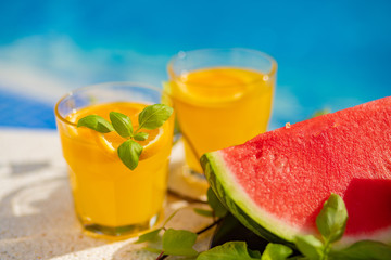 Summer holiday tropical concept. Fresh orange juice and watermelon juice and pineapple on border of a swimming pool.