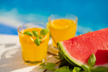 Summer holiday tropical concept. Fresh orange juice and watermelon juice and pineapple on border of a swimming pool.