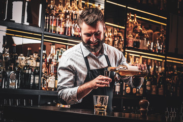 Diligent happy barman is preparing alcoholic beverege for customer.