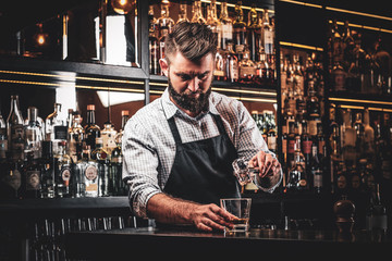 Diligent serious barman is preparing alcoholic beverege for customer.