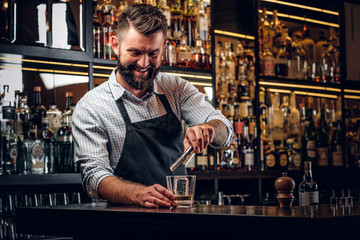 Happy smiling barman is prepairing drinks for customers at posh bar.