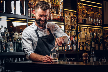 Happy smiling barman is prepairing drinks for customers at posh bar.
