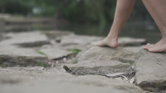 Woman walking barefoot on the rocks by the river or lake during a sunny day. Slow motion Female feet strolling at the nature. Freedom alone scene and relax time concept meditate