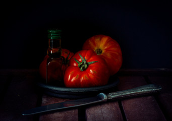 RED TOMATOES WITH OLIVE OIL AND ANTIQUE KNIFE ON WOODEN TABLE