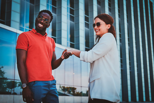 Happy smiling bisness partners in sunglasses meeteng up near glass building at city centre.