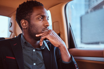 Portrait of pensive elegant afro etnicity businessman in the car as a passenger.