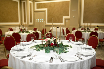 Festively decorated round banquet table in the restaurant. Fresh flowers are golden candles and red chairs. expensively rich