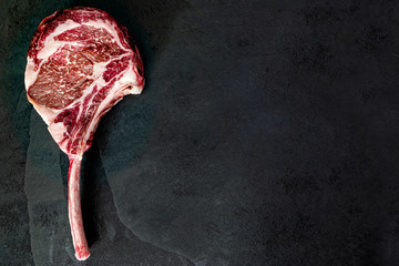 Raw, dry-aged wagyu tomahawk steak on a  black stone table. Top view and copy space