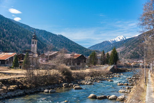The Noce River surrounded by hills with snow-capped mountains - Italian alps. In the distance Pellizzano city, Trento, Trentino, Italy, Europe