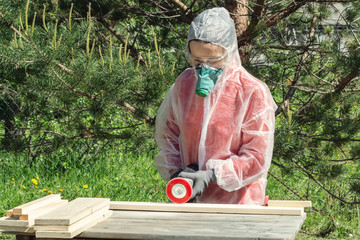Woman carpenter in respirator, goggles and overalls handles a wooden board with a Angle grinder