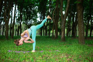 Thin brunette girl plays sports and performs beautiful and sophisticated yoga poses in a summer...